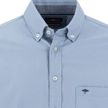 Load image into Gallery viewer, A close-up of a light blue button-down shirt by The Waterman, featuring a classic collar, white buttons, and a chest pocket with a navy embroidered tree logo.
