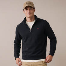 Load image into Gallery viewer, A man wearing a dark navy quarter-zip pullover sweater with a small red embroidered logo on the left chest, styled with a white t-shirt, khaki pants, and a tan baseball cap against a solid beige background.
