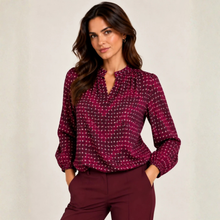 Load image into Gallery viewer, A woman modeling a long-sleeve blouse with a burgundy and magenta base and a small white geometric pattern, paired with matching burgundy trousers, against a neutral light beige background.

