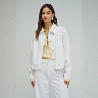 Woman wearing a white denim jacket and white pants on a gray background