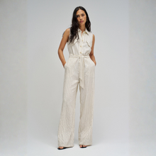 Load image into Gallery viewer, A woman modeling a sleeveless, wide-leg pinstripe jumpsuit in cream and beige. The jumpsuit features a button-down front, a matching fabric tie belt at the waist, and side pockets, photographed against a neutral light gray studio background.
