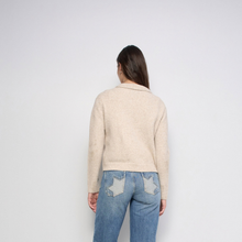 Load image into Gallery viewer, A woman viewed from behind wearing a light beige knit sweater and blue jeans with star-shaped patch pockets, standing against a plain light gray studio background.

