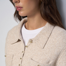 Load image into Gallery viewer, Close-up of a woman wearing a light beige textured knit cardigan with gold-tone buttons over a white crewneck t-shirt.
