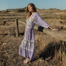 Load image into Gallery viewer, Woman in a purple dress standing by a wooden fence in a desert landscape

