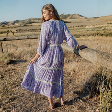Load image into Gallery viewer, Woman in a purple dress standing in a field with a wooden fence and hills in the background
