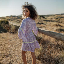 Load image into Gallery viewer, Woman in a purple dress standing in a desert landscape with a wooden fence.
