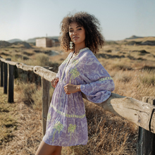 Load image into Gallery viewer, Woman in a purple dress standing by a wooden fence in a desert landscape
