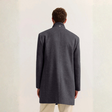 Load image into Gallery viewer, A man viewed from behind wearing a dark charcoal gray wool-blend coat with a high stand collar and light beige trousers, set against a neutral off-white textured background.
