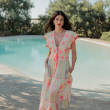 Load image into Gallery viewer, Woman in a colorful embroidered dress standing by a pool with trees in the background
