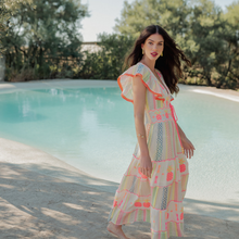 Load image into Gallery viewer, Woman in a colorful dress standing by a pool with trees in the background
