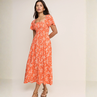 Woman wearing an orange floral dress against a plain background