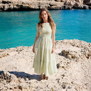 Woman in a light dress standing on rocky terrain with turquoise water and cliffs in the background