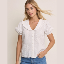 Load image into Gallery viewer, Woman wearing a white blouse with ruffled collar and blue jeans on a beige background
