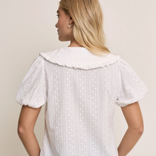 Load image into Gallery viewer, Woman wearing a white blouse with ruffled collar and short sleeves on a beige background
