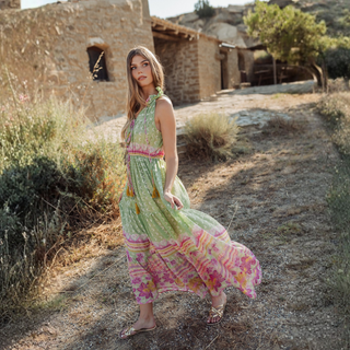 Woman in a colorful dress standing on a dirt path with rustic buildings in the background