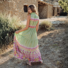 Load image into Gallery viewer, Woman in a colorful dress standing in a rustic outdoor setting.
