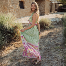 Load image into Gallery viewer, Woman in a long, patterned dress standing in a rustic outdoor setting.
