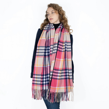 Load image into Gallery viewer, A woman modeling a large plaid scarf with pink, navy, beige, and yellow stripes and fringed ends, worn over a dark navy top and blue jeans against a plain white background.

