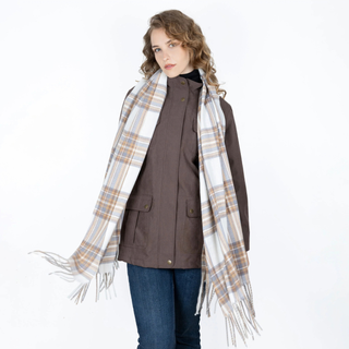 A woman modeling a brown jacket and blue jeans, wrapped in a large cream, beige, and brown plaid fringed scarf against a plain white background.
