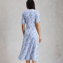 Load image into Gallery viewer, Woman wearing a blue and white patterned dress against a gray concrete wall.
