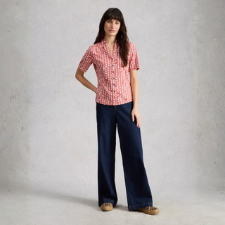 Woman wearing a red patterned shirt and blue jeans against a plain background