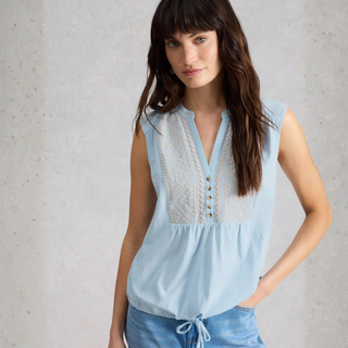 Woman wearing a light blue sleeveless top with intricate details against a neutral background