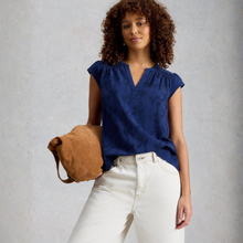 Load image into Gallery viewer, Woman wearing a blue top and white pants, holding a brown bag against a gray background
