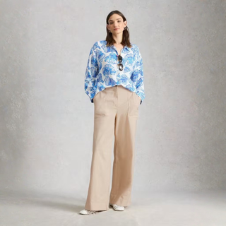 Woman wearing a blue floral blouse and beige pants against a gray background