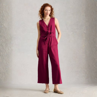 Model wearing magenta linen jumpsuit on grey background.