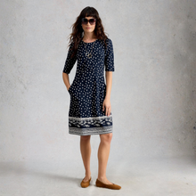 Load image into Gallery viewer, Woman wearing a navy dress with white polka dots and patterned hem against a gray background

