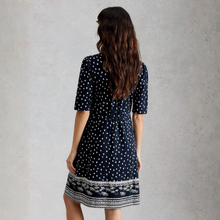 Load image into Gallery viewer, Woman wearing a black dress with white polka dots and a patterned hem against a gray background
