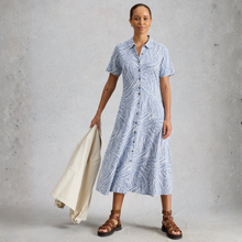 Load image into Gallery viewer, Woman wearing a blue patterned dress holding a beige jacket against a gray background
