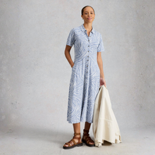 Load image into Gallery viewer, Woman wearing a blue patterned dress holding a white jacket against a gray background
