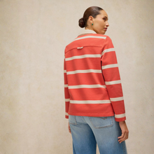 Load image into Gallery viewer, A woman shown from the back wearing a coral red and white horizontally striped long-sleeve knit top with a small chest pocket, paired with light blue jeans, against a textured beige studio background.

