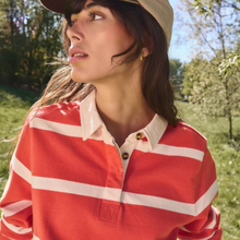 Load image into Gallery viewer, A woman outdoors wearing a red and white horizontally striped long-sleeve polo shirt with a beige cap, photographed in a sunny grassy park setting.
