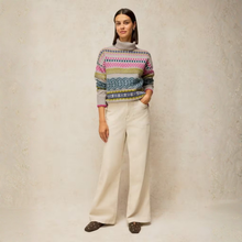 Load image into Gallery viewer, A woman stands against a textured beige studio backdrop wearing a multicolor Fair Isle patterned knit sweater with a gray turtleneck, off-white wide-leg trousers, and dark brown pointed flats.
