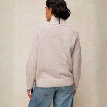 Load image into Gallery viewer, A person shown from the back wearing a light grey knit sweater with tiny multicolor flecks and blue jeans, standing against a textured beige wall.
