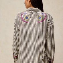 Load image into Gallery viewer, A woman shown from the back wearing a vertically striped button-up shirt with colorful embroidered details on the shoulders and cuffs.
