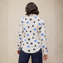 Load image into Gallery viewer, A person shown from the back wearing a cream-colored long-sleeve button-up shirt with a pattern of hand-drawn blue and black polka dots, paired with dark blue jeans, against a neutral beige background.
