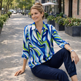 Woman wearing a colorful patterned shirt sitting on a street.