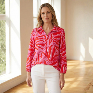 Woman wearing a pink patterned blouse and white pants in a bright room.