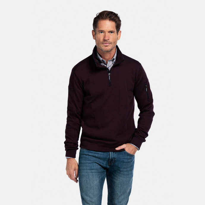 Man wearing a dark brown half-zip sweater and blue jeans on a white background