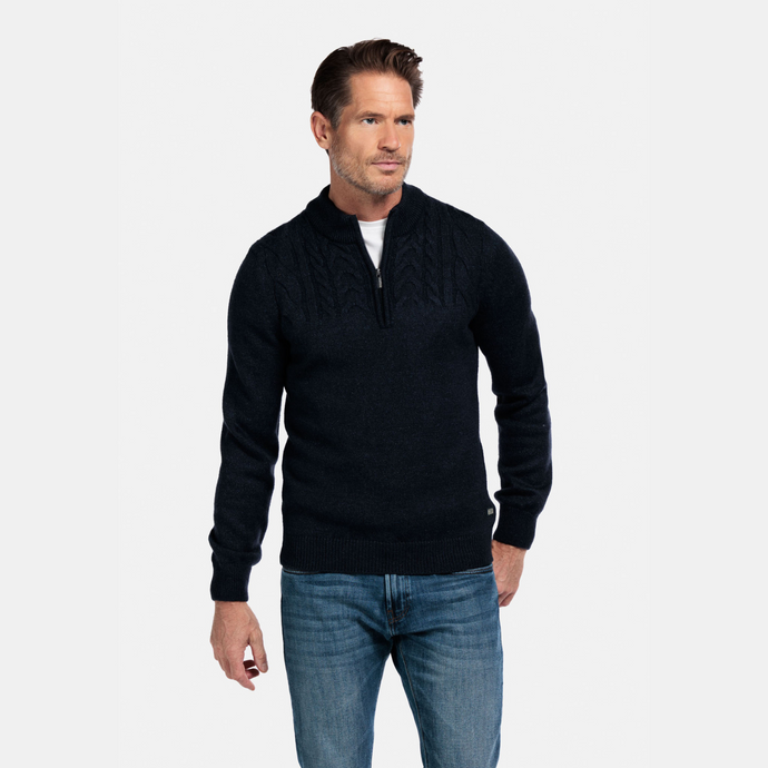 Man wearing a black quarter-zip sweater and blue jeans on a light gray background