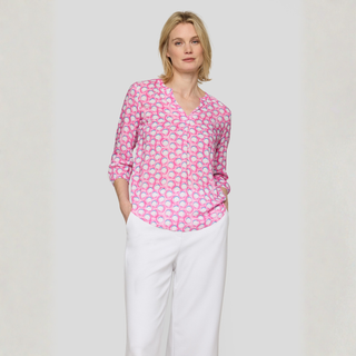 Woman wearing a pink patterned blouse and white pants on a plain background
