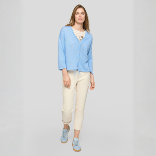 Woman wearing a light blue cardigan and beige pants on a gray background