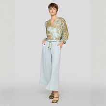 Load image into Gallery viewer, Woman wearing a patterned blouse and light blue pants on a white background
