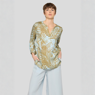 Woman wearing a patterned blouse and light pants on a plain background