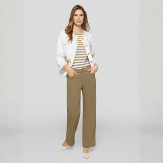 Woman wearing a white jacket, striped shirt, and brown pants on a gray background