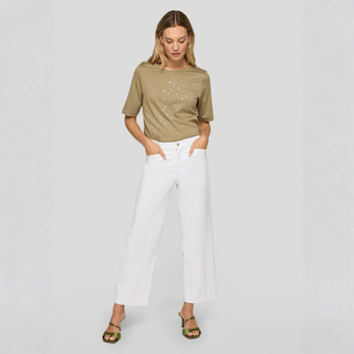 Woman wearing a green t-shirt and white pants on a light gray background