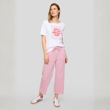 Load image into Gallery viewer, Woman wearing a white t-shirt with red text and pink checkered pants on a gray background
